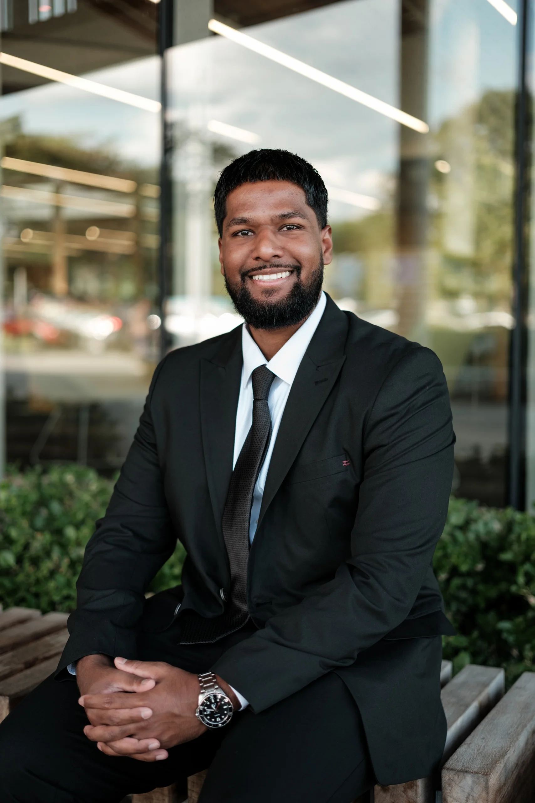 Relaxed corporate headshot of a smiling man in a black suit seated outdoors in Toronto, by AD Photography