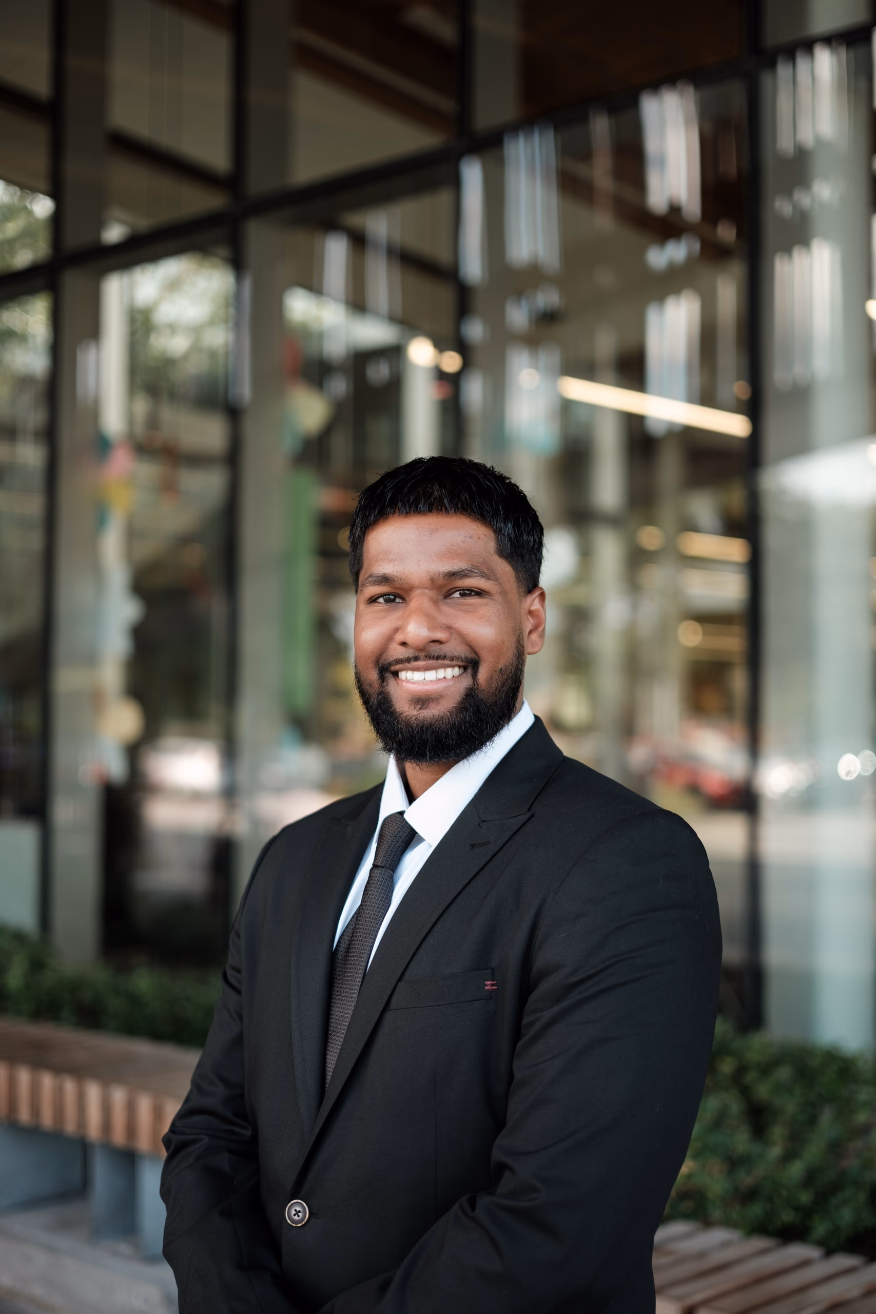 Professional LinkedIn headshot of a smiling man in a black suit outside a modern Toronto office building, by AD Photography