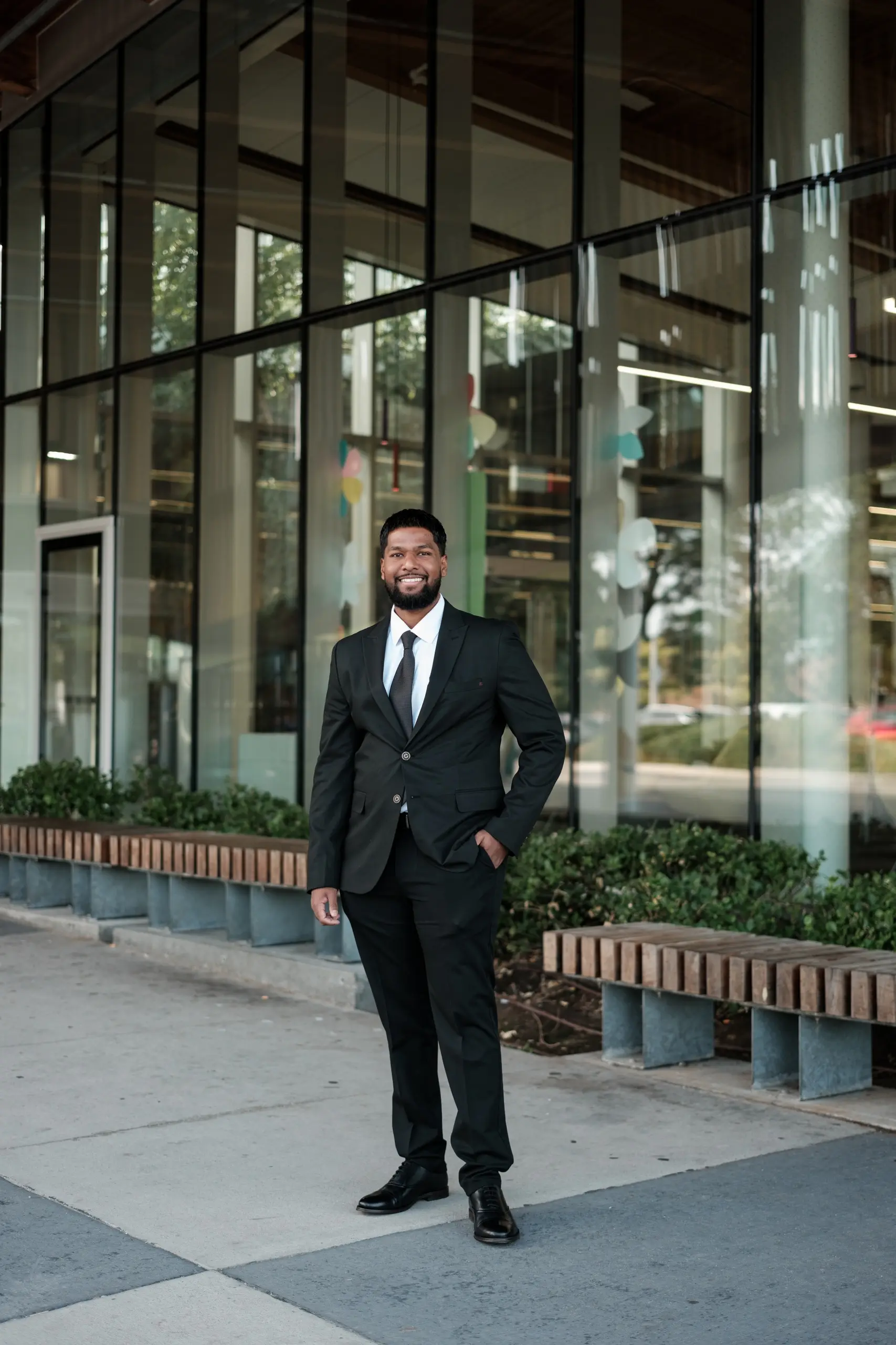 Full length professional portrait of a man in a black suit standing on the sidewalk beside a glass Toronto office building, by AD Photography