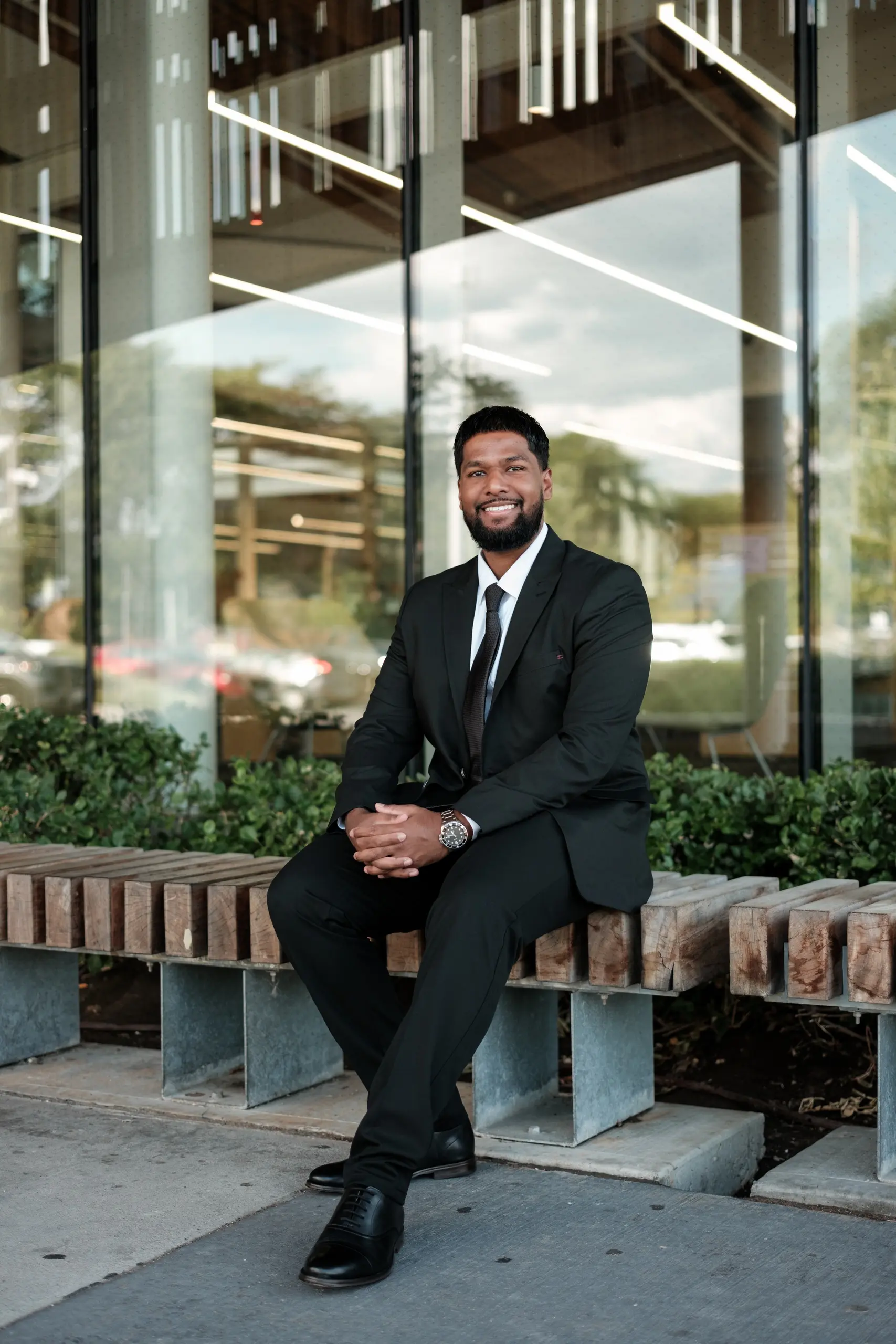 Full length business portrait of a man in a black suit seated on a bench outside a Toronto office building, by AD Photography