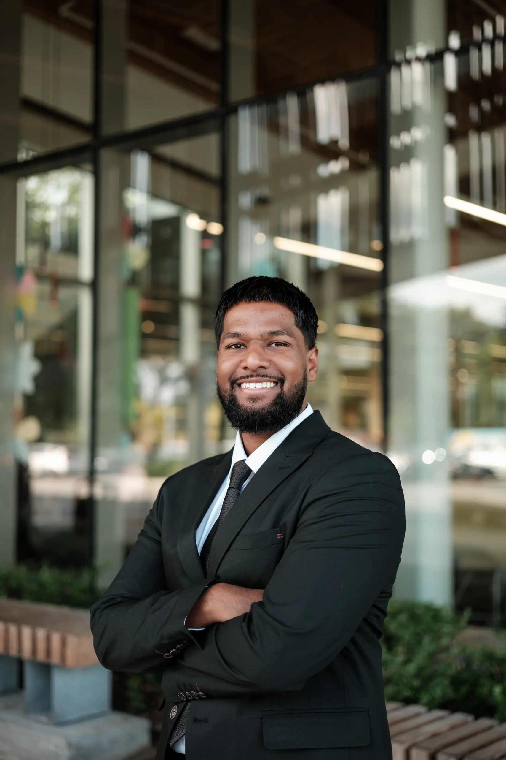 Corporate headshot of a smiling man in a black suit standing with his arms crossed outside a Toronto office