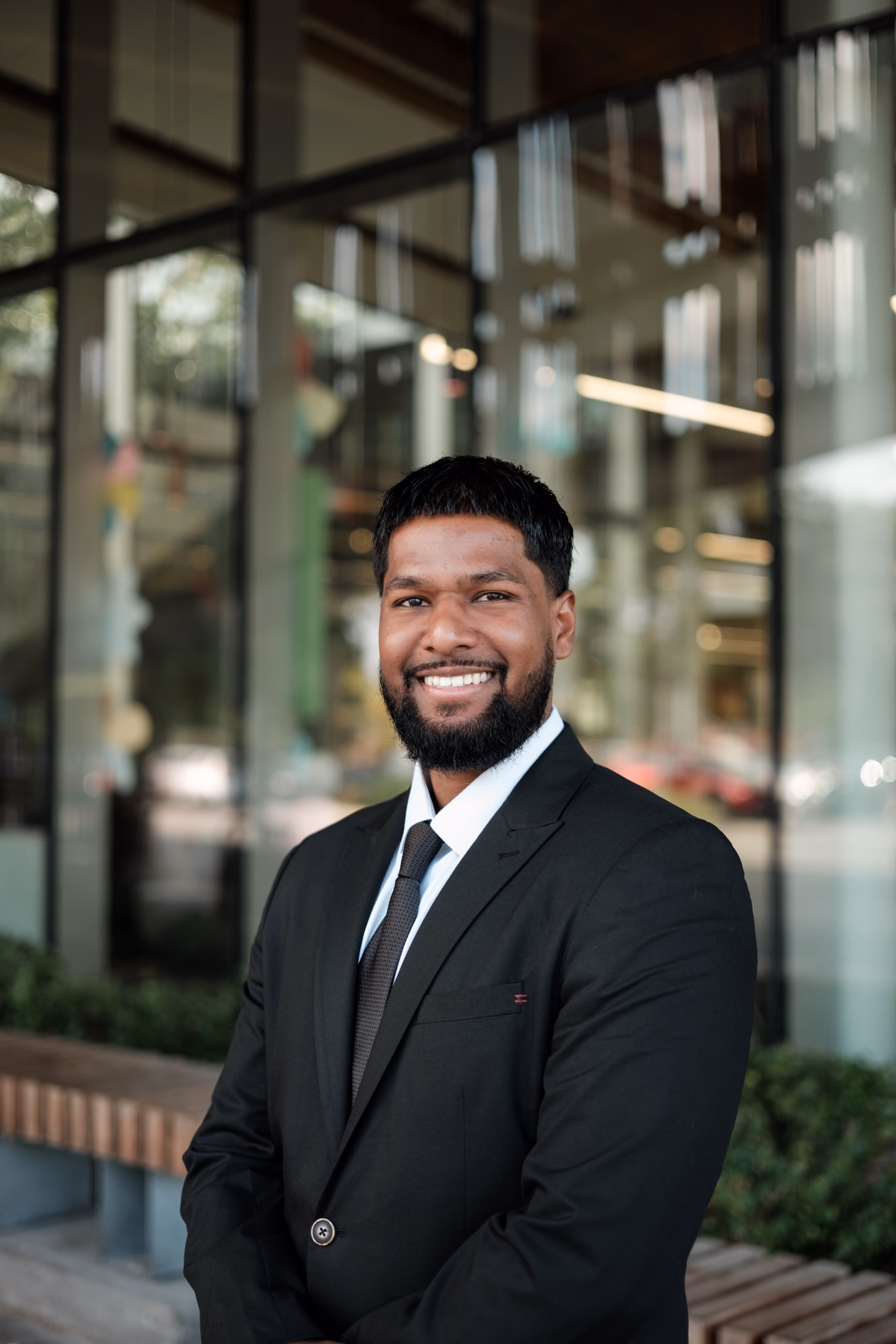 A smiling man in a black suit standing outside a modern Toronto building with his hands in his pockets, by AD Photography