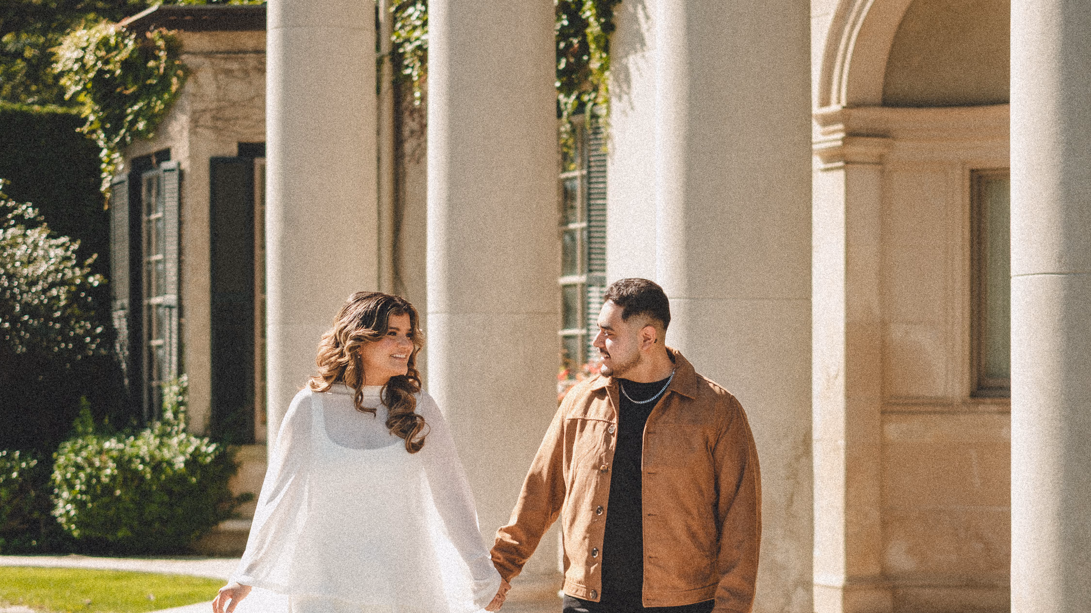 Maninder and Parneet walking hand in hand past the giant stone columns of the Parkwood Estate colonnade, by AD Photography